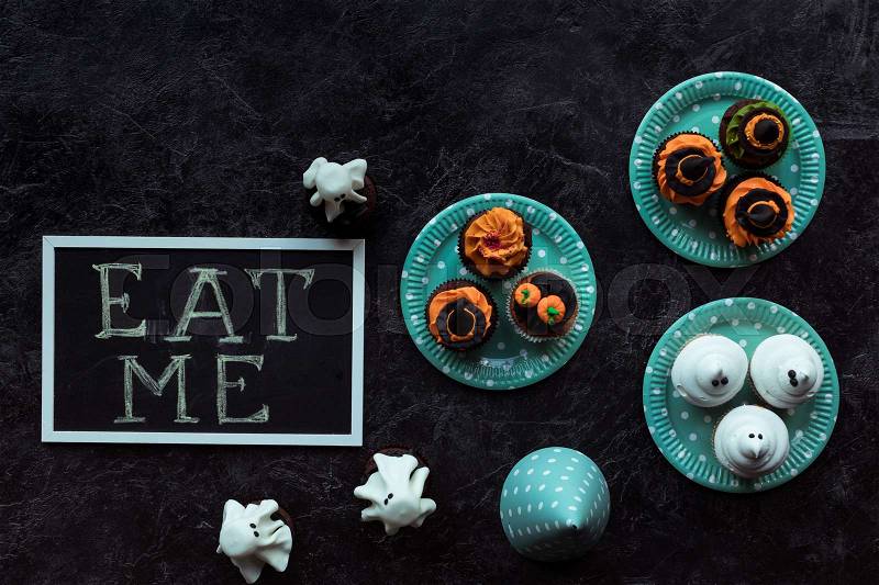 Top view of halloween cupcakes and eat me inscription on black, stock photo