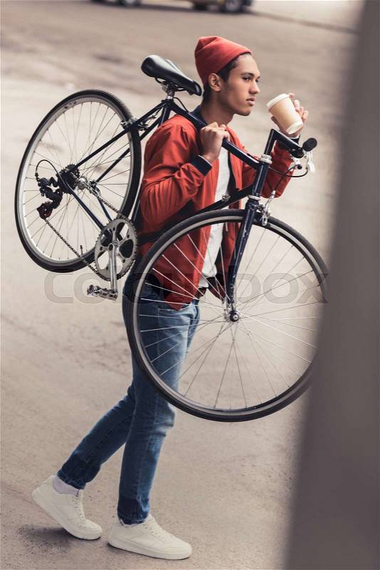 Thoughtful man carrying vintage bicycle and drinking coffee to go, stock photo