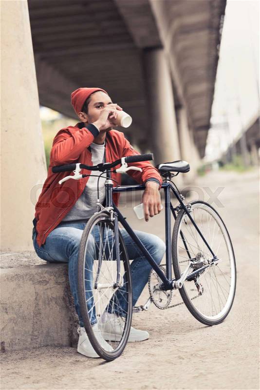 Young man with vintage bicycle drinking coffee to go, stock photo