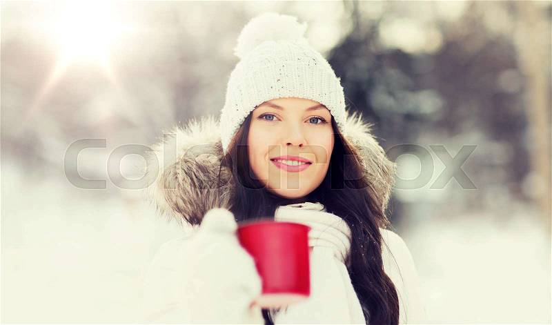 People, season, drinks and leisure concept - happy young woman with tea cup outdoors in winter, stock photo