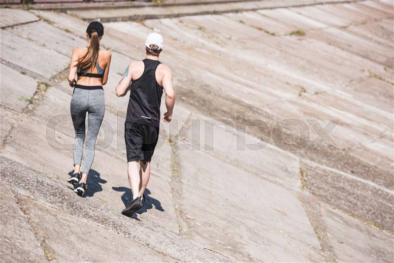 Back view of athletic couple jogging together on slabs, stock photo