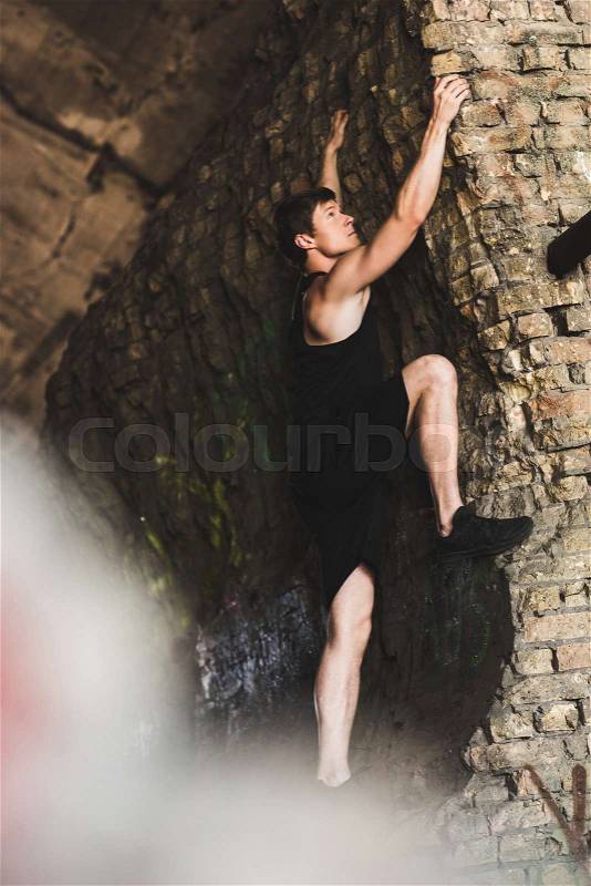 Selective focus of sportive man climbing on ruins, stock photo