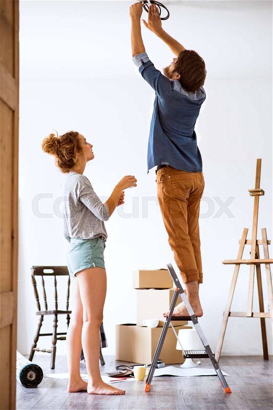Young married couple moving in new house, changing a light bulb, stock photo