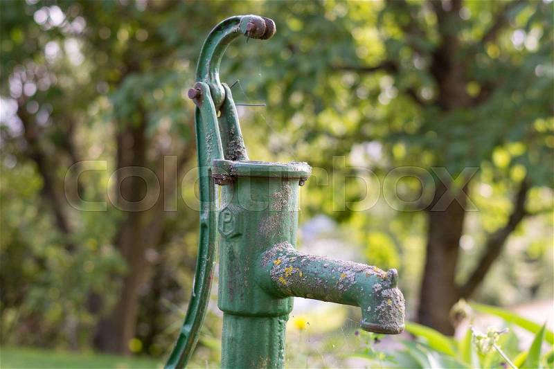 An old green rusty garden pump out of order in the garden, stock photo