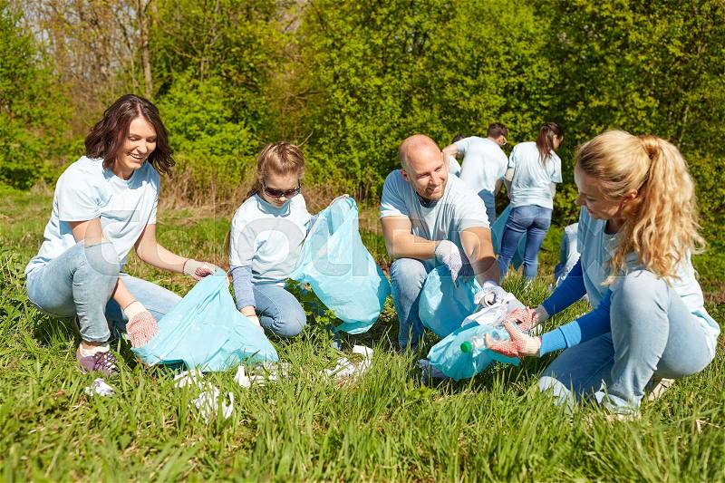 Volunteering, charity, people and ecology concept - group of happy volunteers with garbage bags cleaning area in park, stock photo