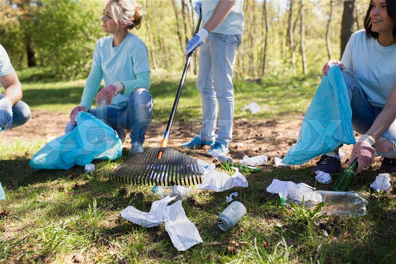 Volunteering, people and ecology concept - group of happy volunteers with garbage bags and rack cleaning area in park, stock photo