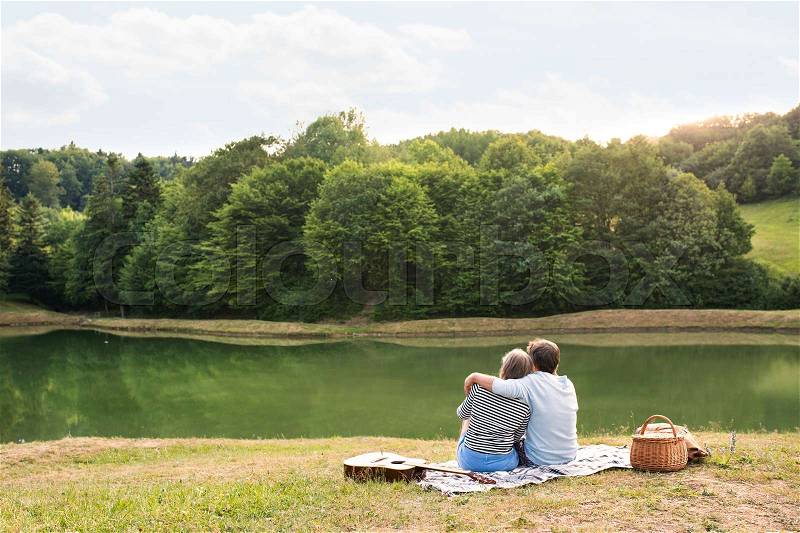 Beautiful senior couple at the lake having a picnic. Green sunny summer nature, stock photo