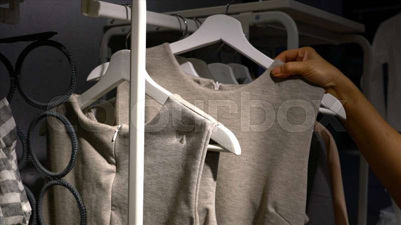 Female hands run across a rack of dress in the closet, browsing in a boutique. , stock photo