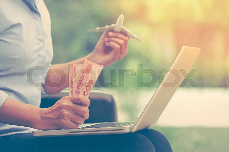 Young business woman using laptop computer and holding airplane with money. travel concept, stock photo