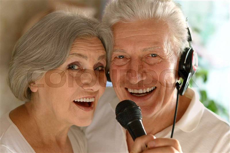 Portrait of happy senior couple singing karaoke, stock photo