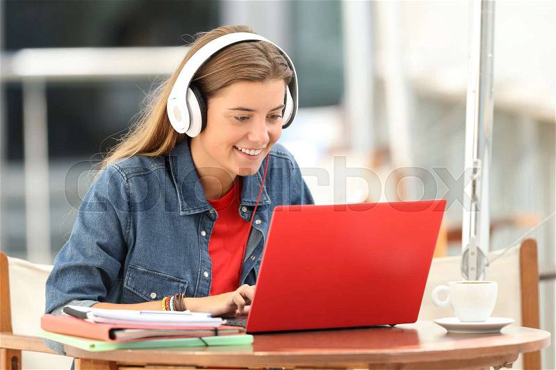 Happy student listening a video tutorial on line with a laptop sitting in a bar terrace, stock photo