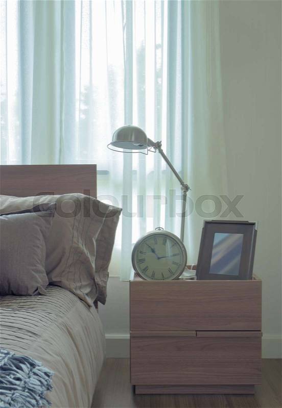 Reading lamp, clock and picture frame on bedside table next to bed, stock photo