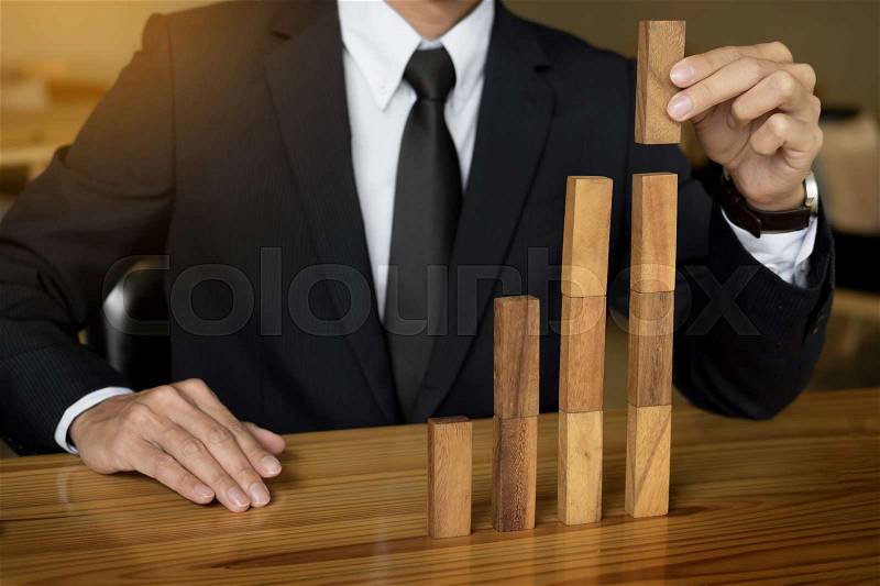 Concept growing value. hand of businessman pick up a wooden block like bar graph growth, stock photo