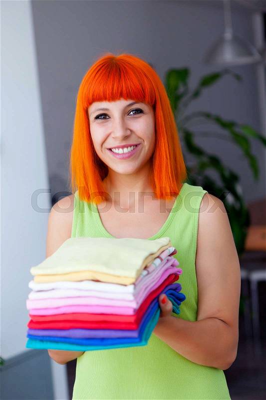 Redhead woman doing laundry with clothes folded and ironed, stock photo