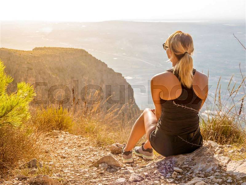 Young women sits at the top of a mountain and looking down on the world. Morning sunrise. Yellow light, stock photo