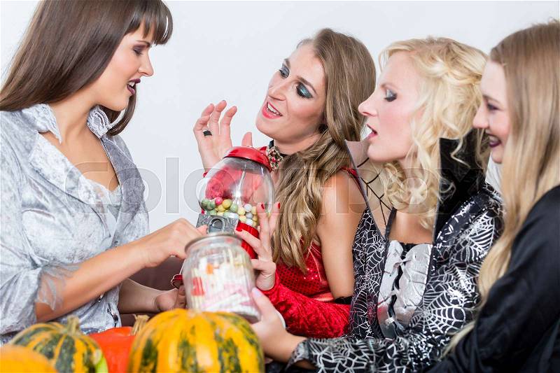 Funny young women and best friends sharing various delicious candies while celebrating Halloween together at costume party indoors, stock photo