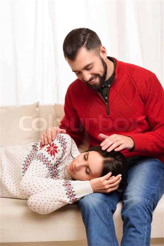 Beautiful young woman sleeping on knees of smiling boyfriend at home, stock photo