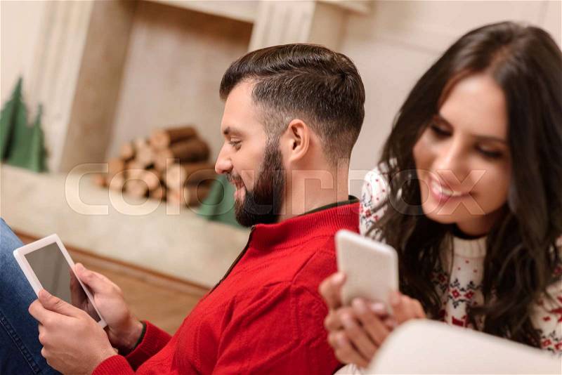 Happy young couple using digital devices at home, stock photo