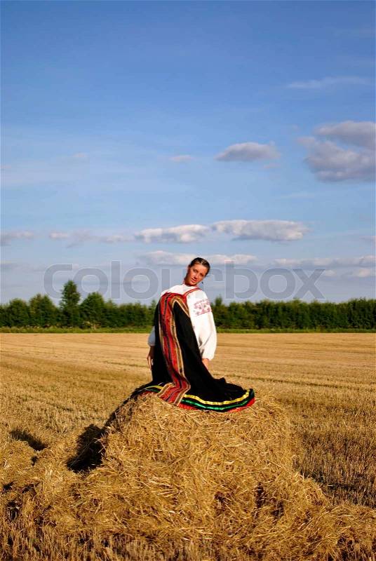 Girl in traditional Russian costume sitting on a haystack, space for text, stock photo