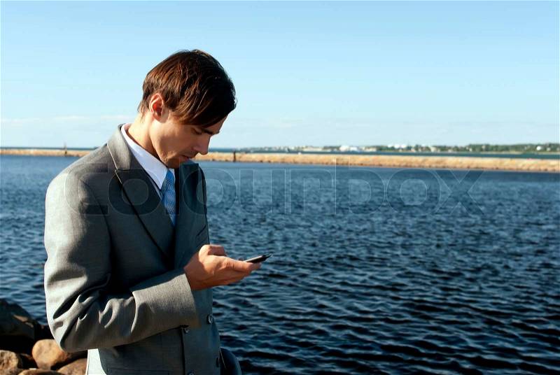Man in a gray suit dials the phone against the sea, stock photo