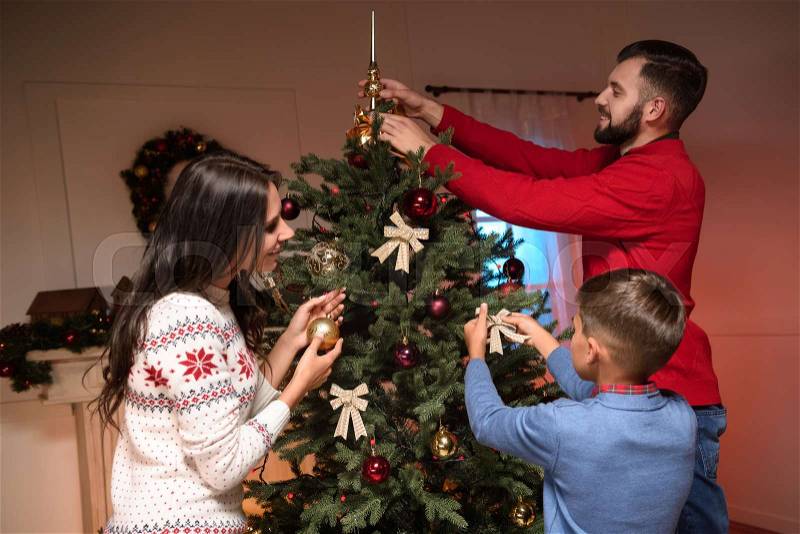 Family decorating christmas tree together at home, stock photo