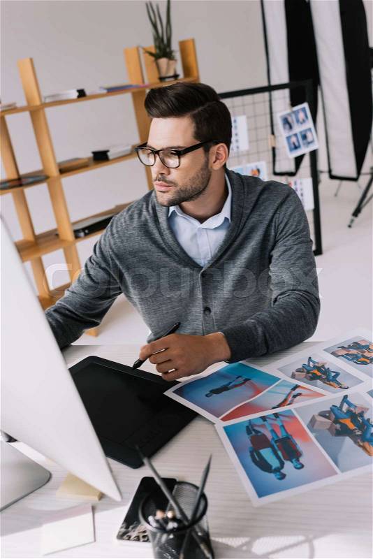 Male photographer working with computer, graphics tablet and photos in modern office, stock photo