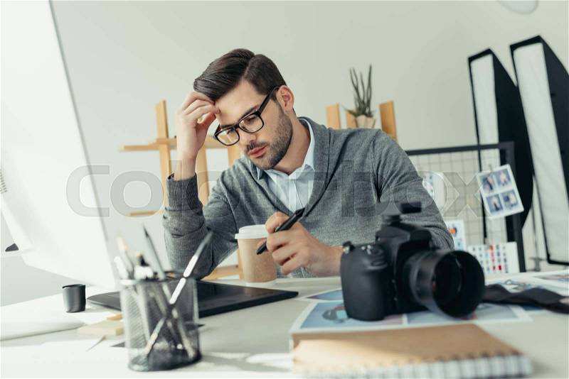 Tired male photographer working with graphics tablet in modern office, stock photo