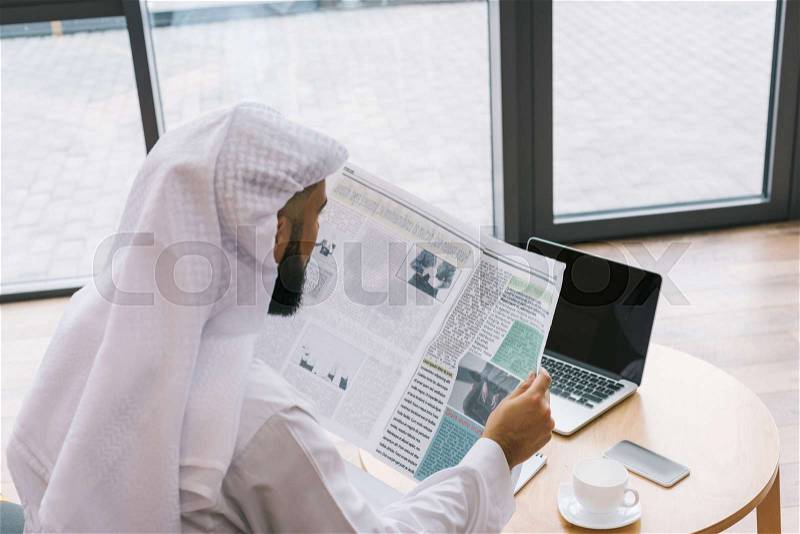 Muslim businessman reading newspaper in modern office, stock photo