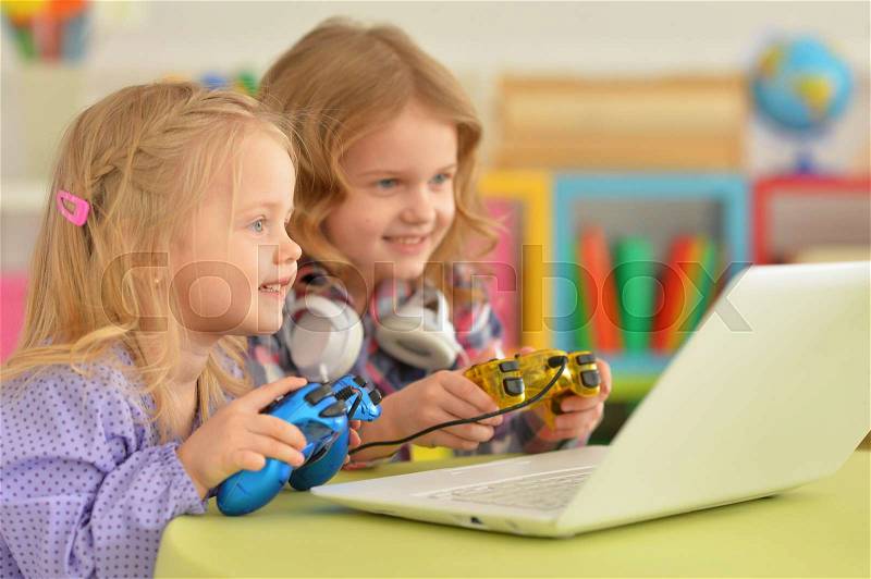 Cute little girls playing computer game on laptop, stock photo