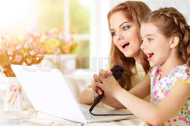 Mother and daughter sitting at table and singing karaoke together, stock photo