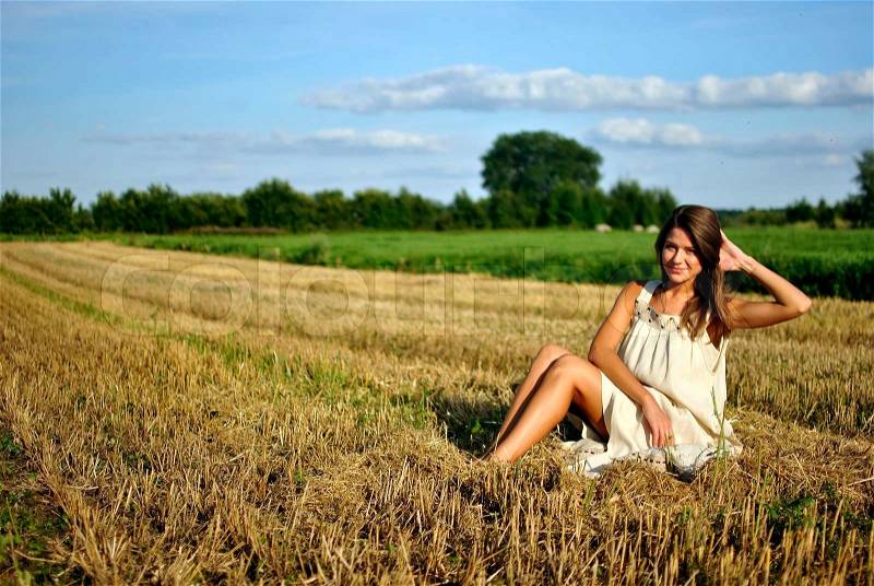 Nice girl in national dress, sitting on a field in rural areas, space for text, stock photo