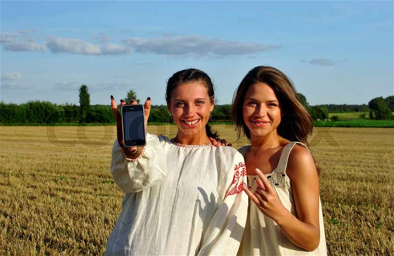 Two girls in a rural clothing show mobile phone into camera, stock photo