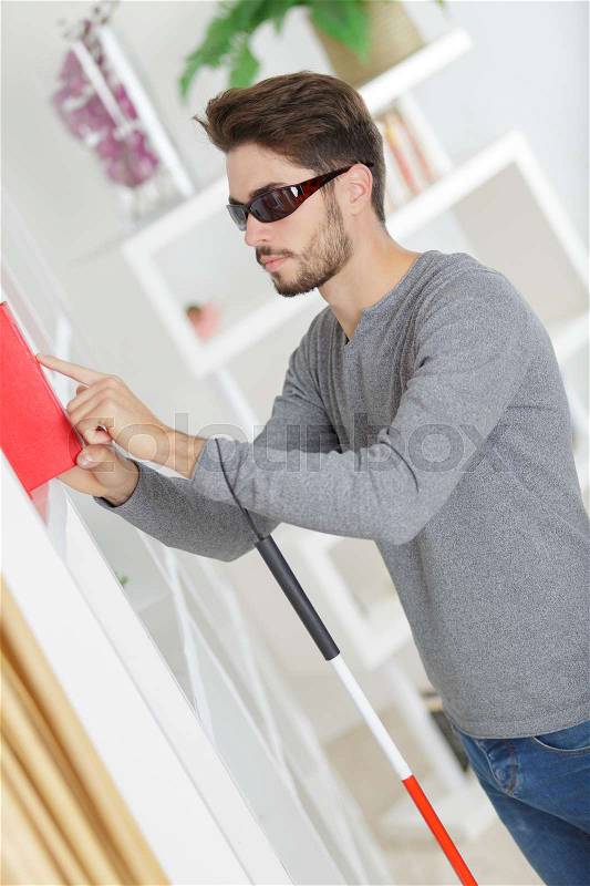 Blind man with white stick and dark glasses at home, stock photo