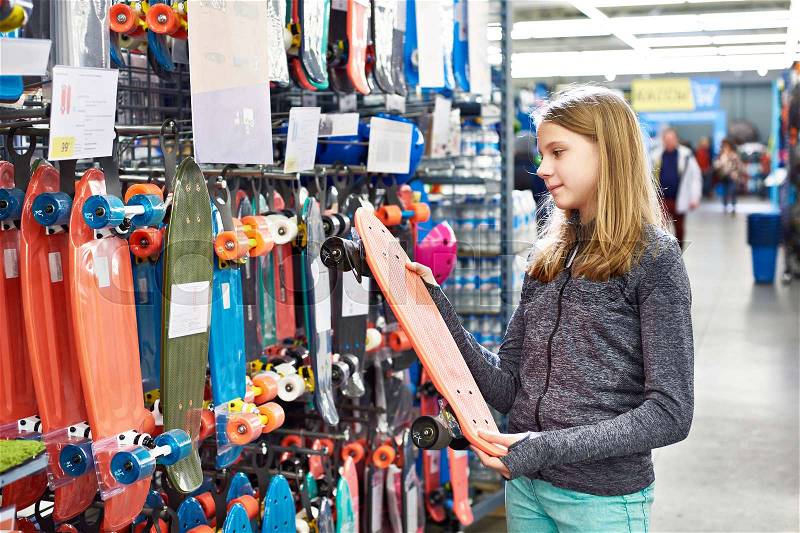 Teenage girl chooses a skateboard in a sports store, stock photo