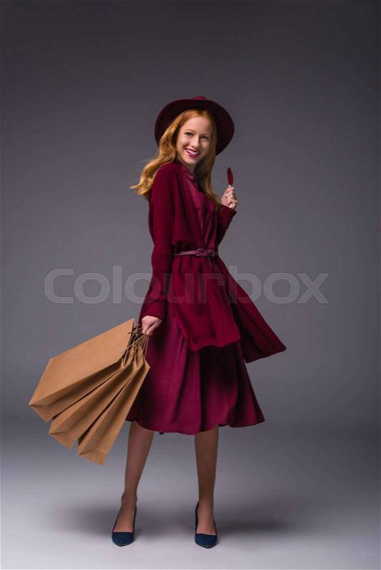 Redhead elegant lady with shopping bags and heart shaped lollipop, on grey, stock photo
