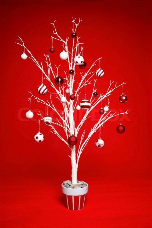 White modern Christmas tree decorated with various red and white themed christmas baubles balls on a red background, stock photo