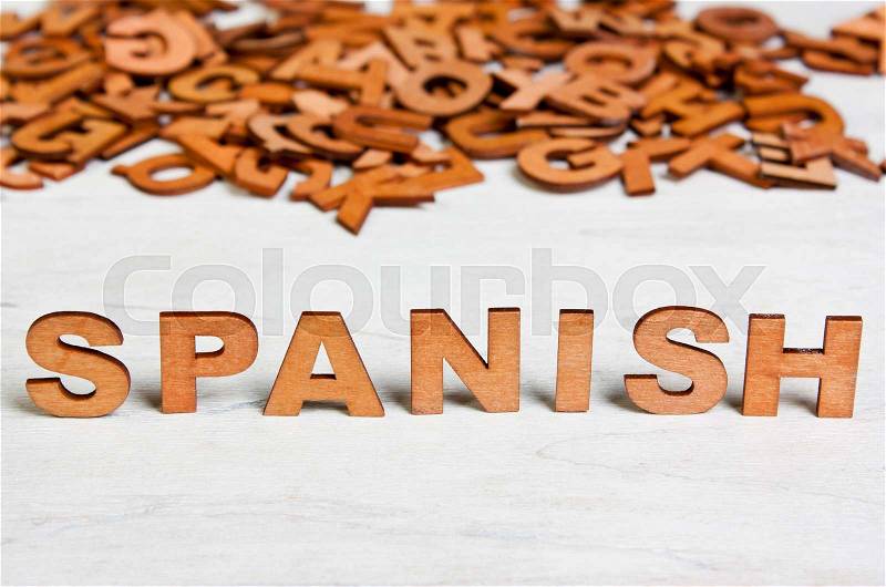 Word Spanish made with wooden letters on a background of other blurred letters, stock photo