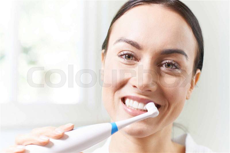 Woman Brushing Teeth With Electric Toothbrush In Bathroom, stock photo