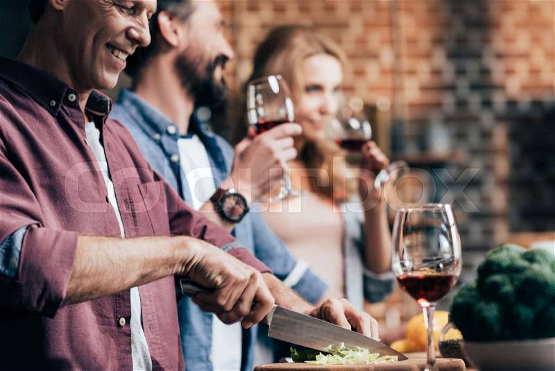 Side view of friends drinking wine while cooking dinner together, stock photo