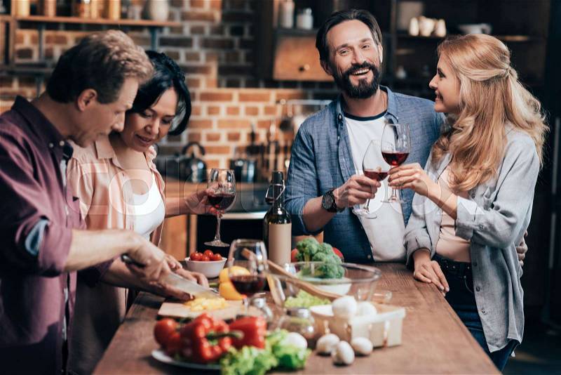 Happy multiethnic friends drinking wine and preparing dinner together, stock photo
