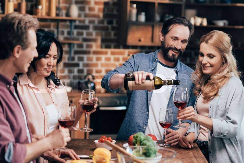 Happy bearded man pouring wine to smiling friends, stock photo