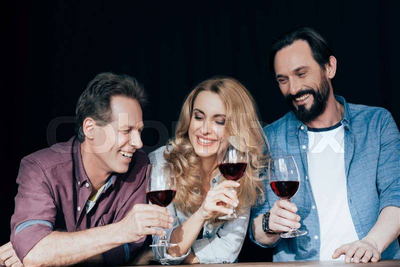 Happy middle aged friends drinking wine and laughing together on black, stock photo