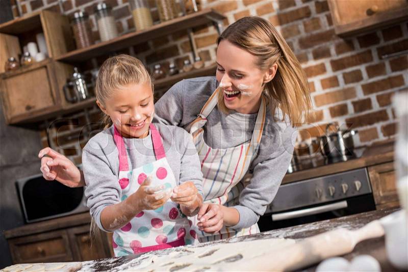 Happy mother and daughter having fun while making cookies together at home, stock photo
