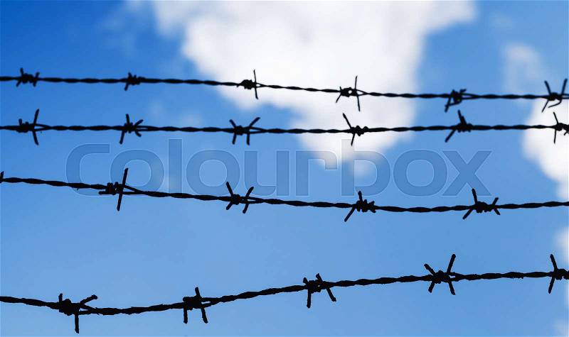Black barbed wire fence over cloudy blue sky background, close up photo with selective focus, stock photo