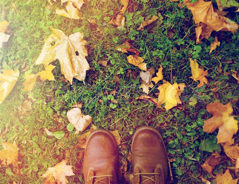 Season, footwear and people concept - feet in boots with autumn leaves on grass, stock photo