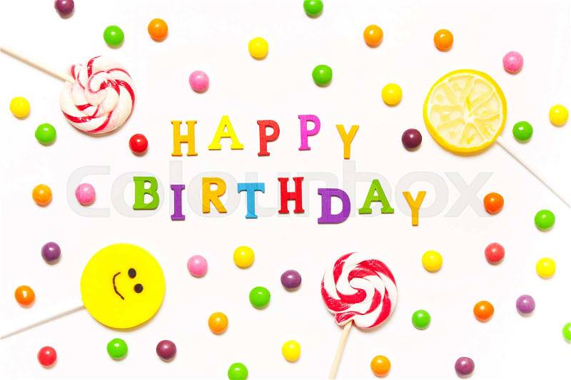 The phrase happy birthday, lollipops, candy smile on, are scattered around the colorful jelly beans on a white background. Top view, flat, stock photo