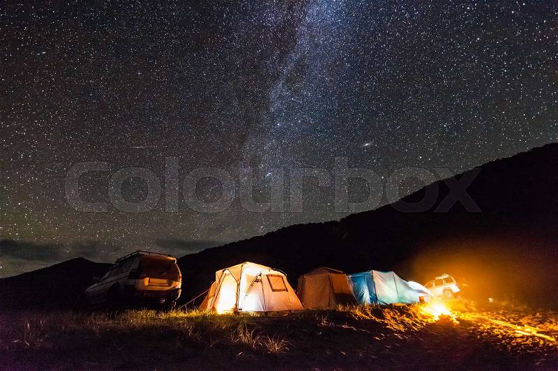 Tourist camping at sea coast at night under starry sky. Some noise from high iso exists, stock photo