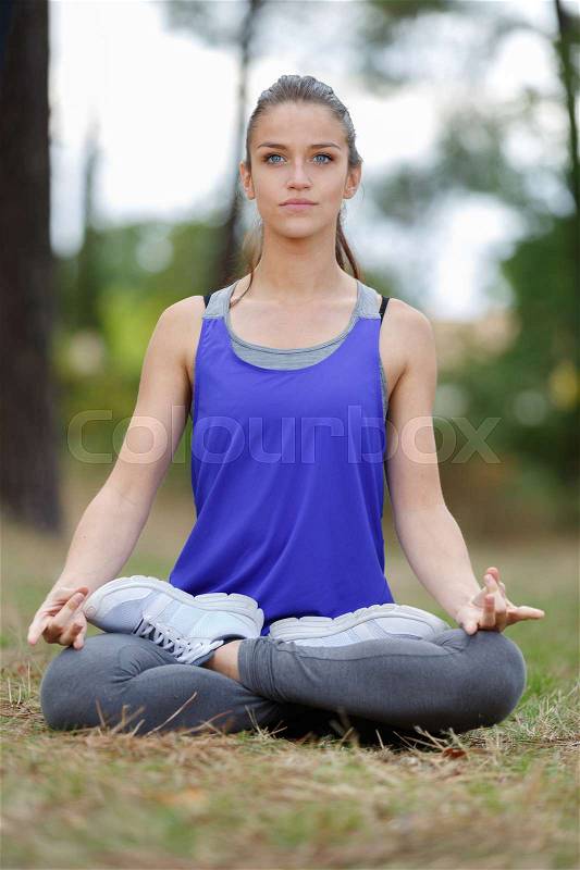 A young woman sitting in yoga lotus pose meditation outdoors, stock photo