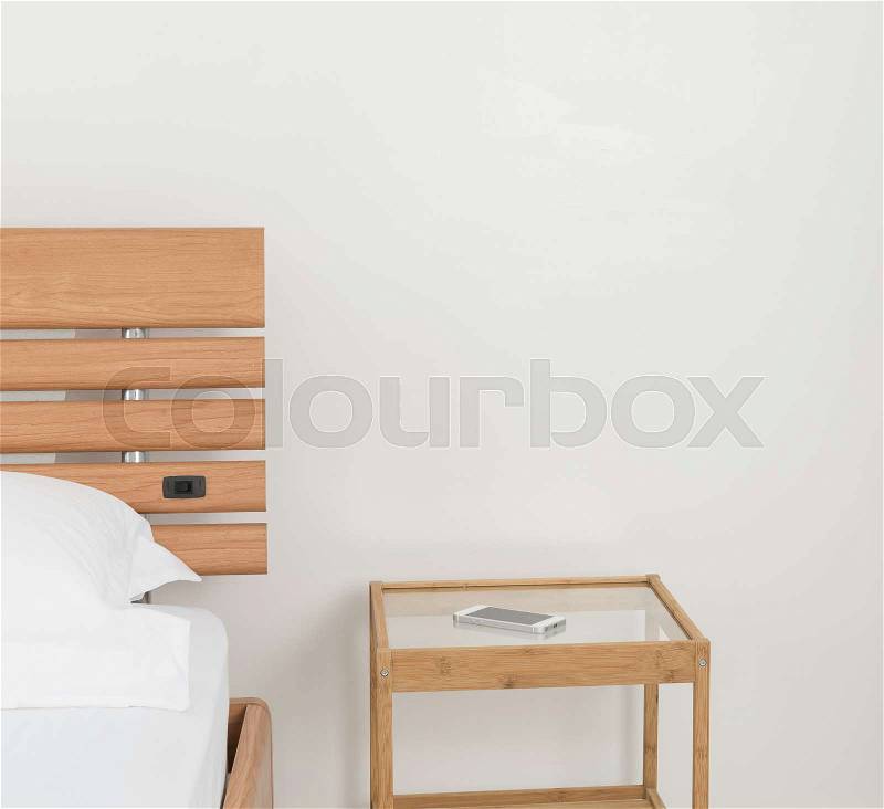 Mobile phone on wooden bed side table decorated in modern white bedroom , stock photo