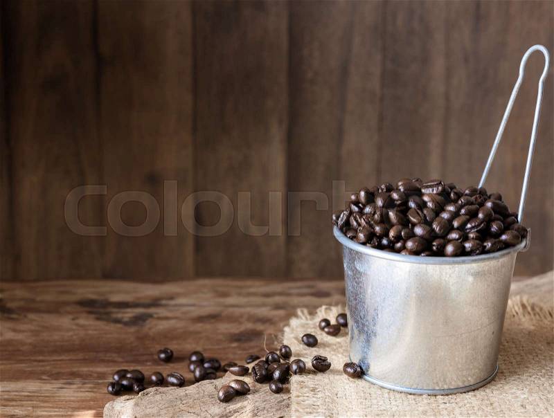 Roasted coffee beans in galvanized can over grunge wooden background, stock photo